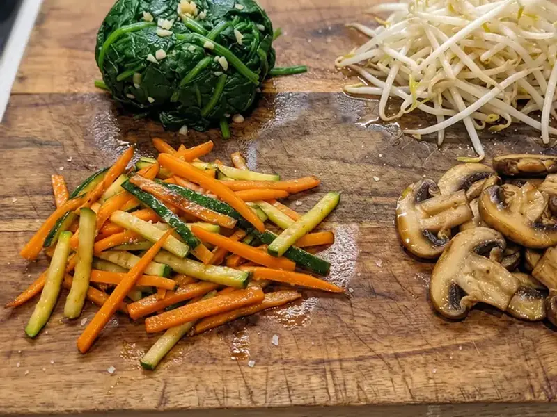 Namul per bibimbap su un tagliere: spinacini, germogli di soia, carota e zucchina a julienne, funghi shiitake a fette