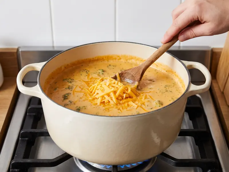 Geriebener Cheddar schmilzt unter dem Siedepunkt in die Brokkolisuppe