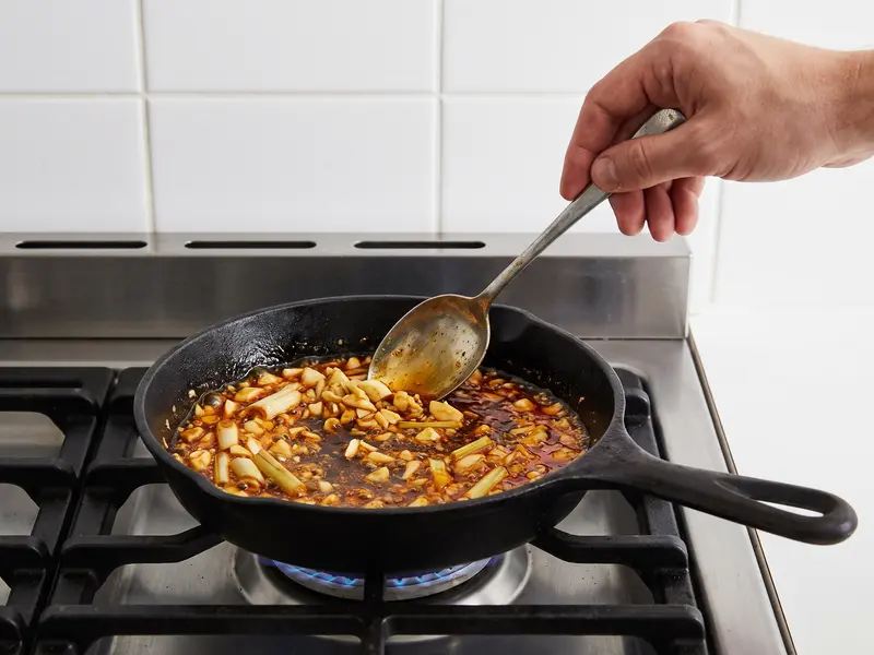 Garlic and lemongrass sizzling in amber chilli oil in a small pan for bun bo hue sate sauce