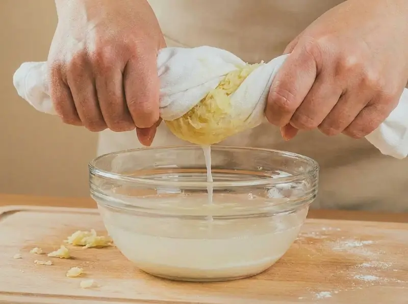 Squeezing grated raw potato in a cloth over a bowl to collect the starch for cepelinai