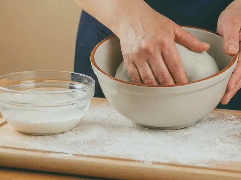 Kneading pale potato dough for cepelinai, a bowl of settled potato starch beside