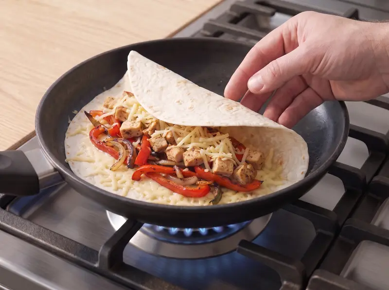 Tortilla in a dry pan with cheese and chicken filling spread over one half