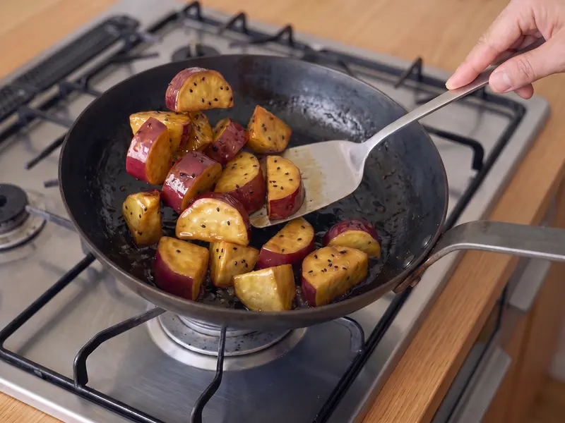 Fried sweet potato chunks tossed in glossy sugar-soy syrup with black sesame in a pan for daigaku imo