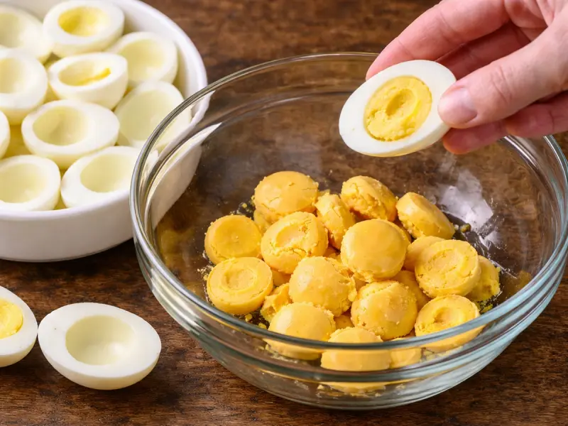 Halved boiled eggs with the yolks popped out into a bowl for deviled eggs