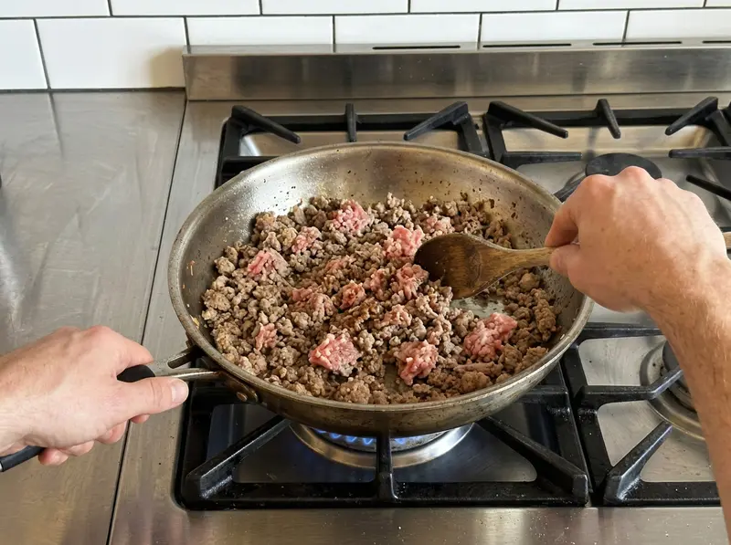 蛋卷碗:木勺在不锈钢煎锅里把正在变色、部分仍是粉色的猪肉末拨散
