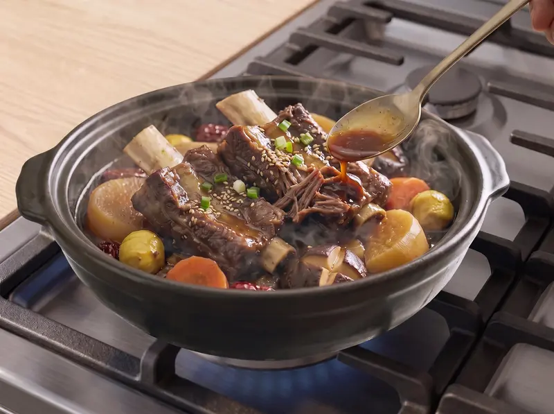 Thickened sauce spooned over galbi-jjim short ribs in a clay pot, topped with sesame and spring onion