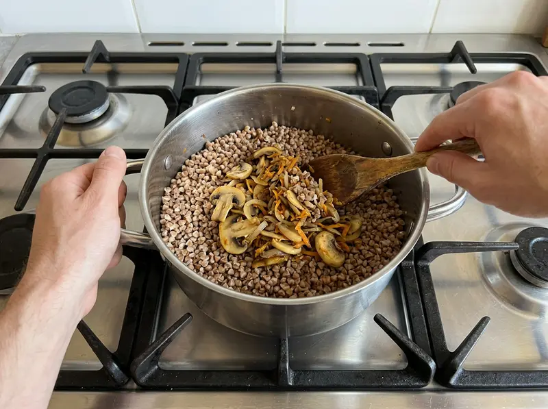Grano saraceno ai funghi: un cucchiaio di legno incorpora funghi fritti, cipolla e carota al grano saraceno sgranato