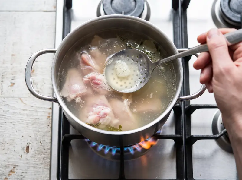 ステンレス鍋で鶏肉を澄んだスープで煮ながら、玉じゃくしで白いアクを取る。緑のボルシチの出汁づくり