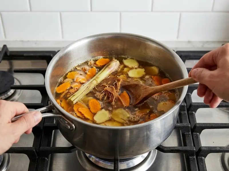 Curcuma e zenzero a fette, citronella e tamarindo sobbollono per il jamu in una casseruola d'acciaio, mescolati col cucchiaio