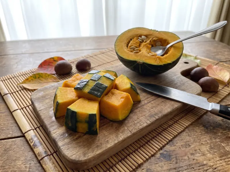 Kabocha pieces for kabocha no nimono on a wooden board, corners trimmed and strips of skin peeled off, knife beside them