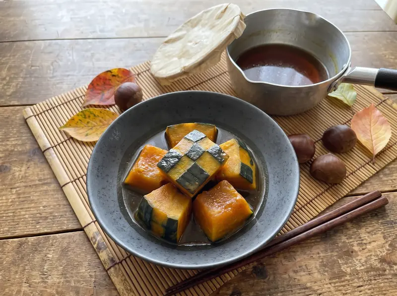 Finished kabocha no nimono in a ceramic bowl with a little glossy dashi broth, skin-side up, chopsticks beside it