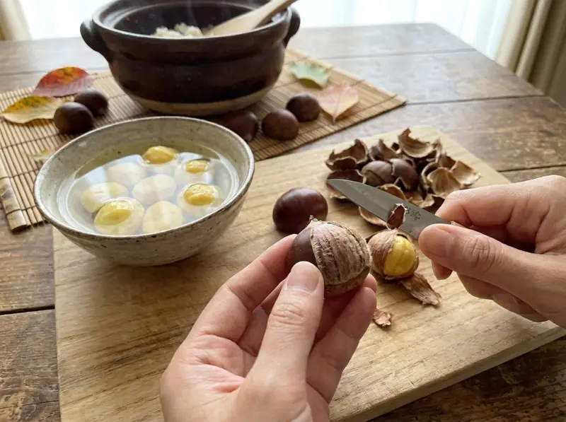 Peeling fresh chestnuts with a small knife for kuri gohan, peeled ones soaking in a bowl of water