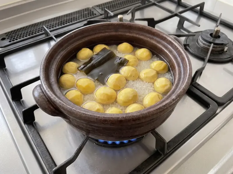 Soaked rice with peeled chestnuts and kombu in a donabe on the gas stove before cooking kuri gohan