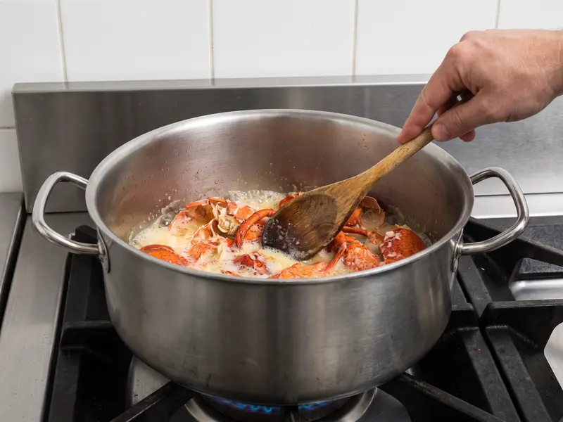Crushed lobster shells turning deep orange-red in foaming butter, pressed down with a wooden spoon, for the lobster bisque