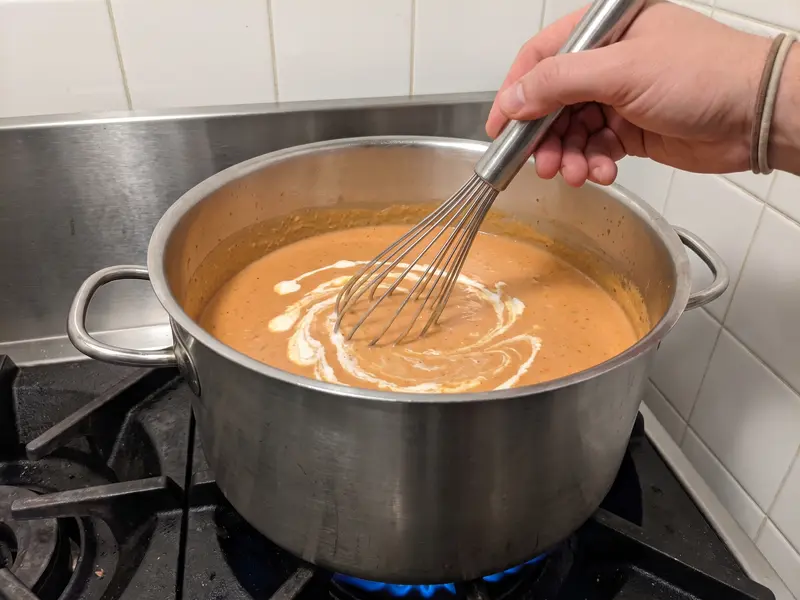 Cream whisked into the lobster bisque, smooth and orange-pink in a steel pot on a gas stove