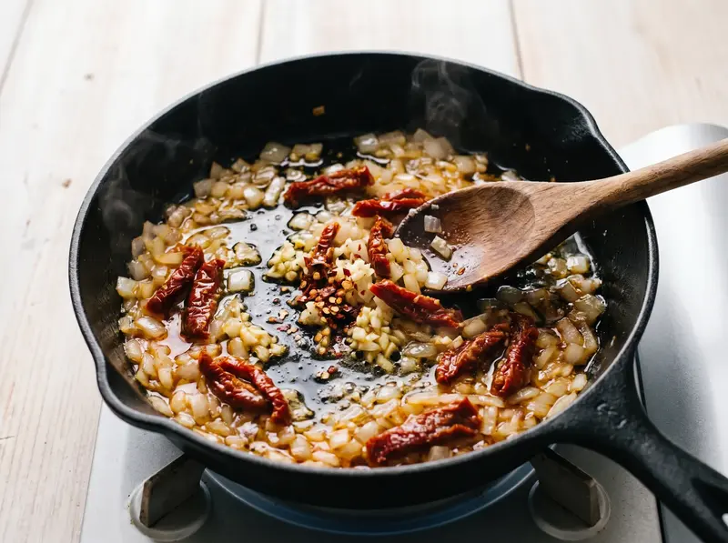 Garlic, sun-dried tomatoes and chilli flakes blooming in oil for marry me beans