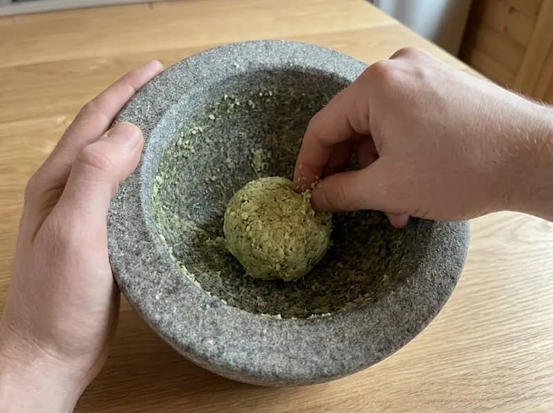 Two fingers gathering the moretum paste from the mortar wall into one rough ball