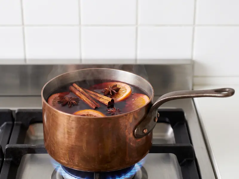 Glühwein dampft sanft mit Orangenscheiben und Kandiszucker über den Gewürzen, ohne zu kochen