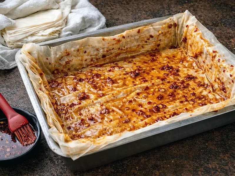 Feuilles de filo superposées dans le plat, badigeonnées de beurre au piment