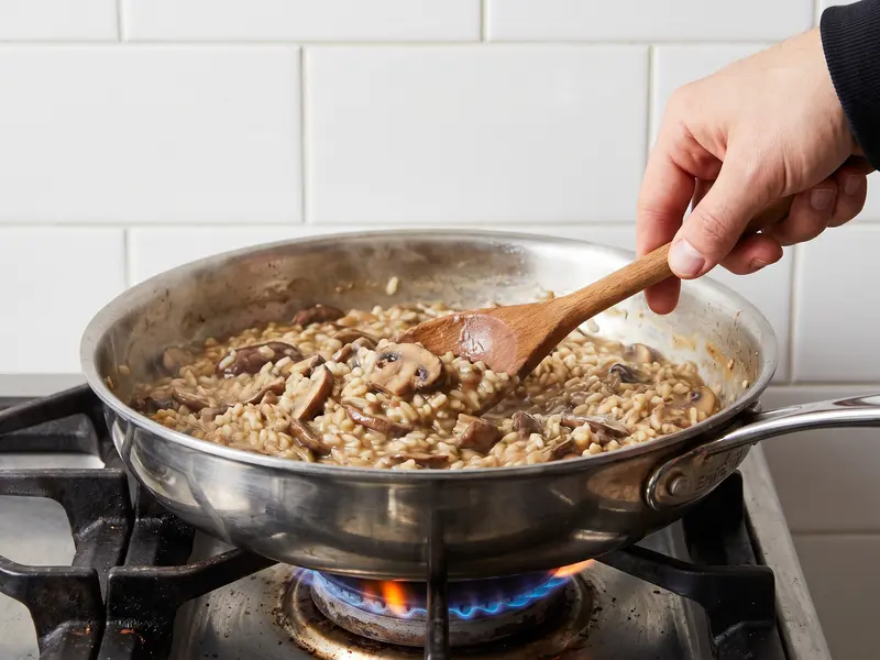 Risotto ai funghi: il riso mescolato col cucchiaio di legno mentre si aggiunge un mestolo di brodo caldo