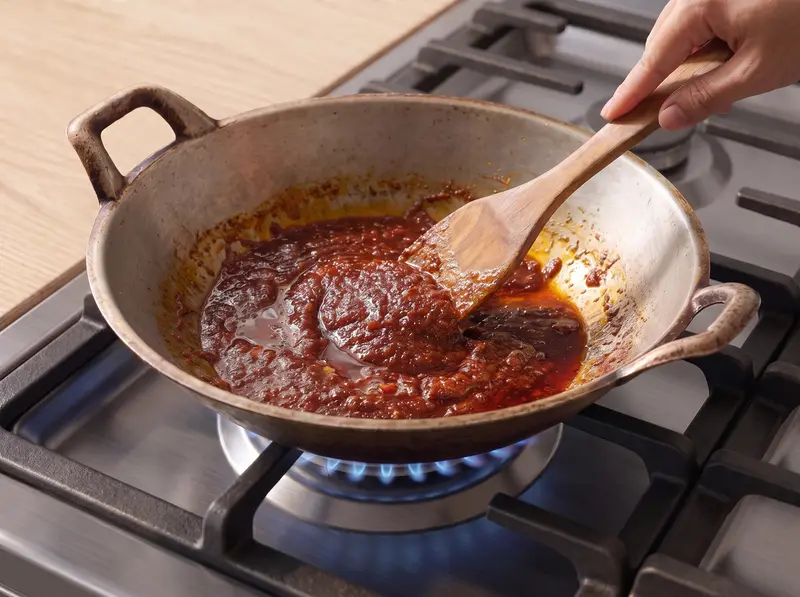 Nasi lemak sambal cooked down to a dark glossy paste in a wok, stirred with a wooden spatula