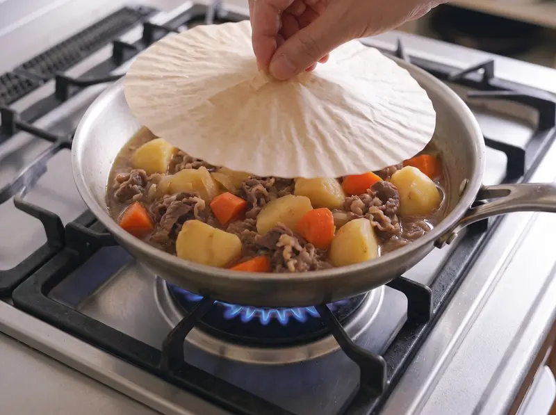 A parchment drop lid laid directly on the simmering nikujaga in the pan on low heat