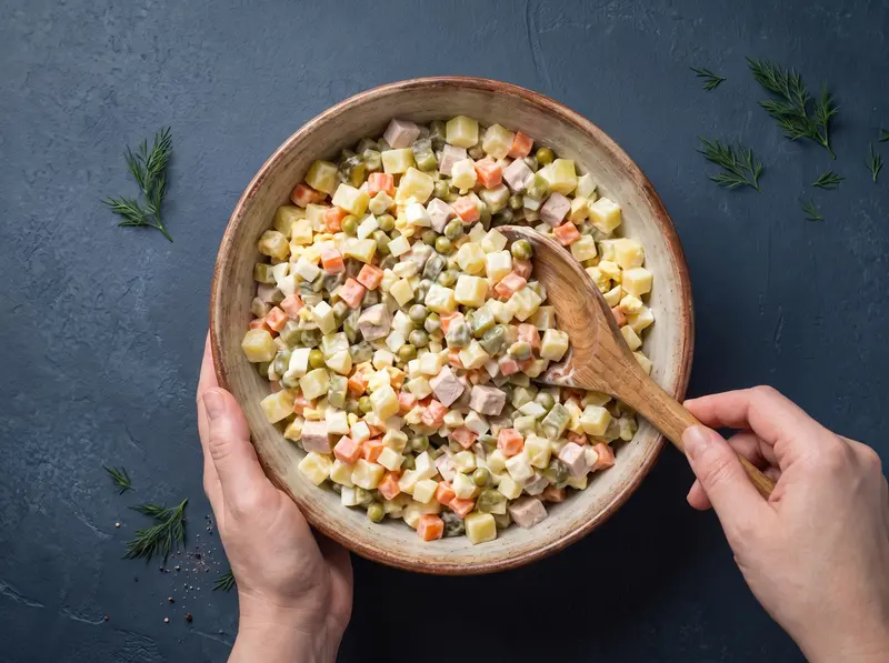 Olivier salad: the diced vegetables, chicken, eggs and peas folded together with mayonnaise dressing in a bowl