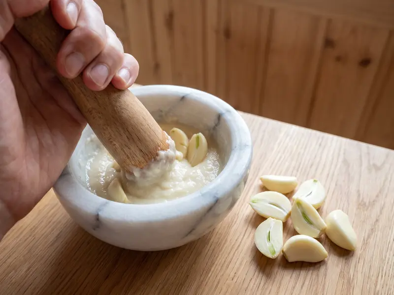 Metà di spicchi d'aglio schiacciate in una pasta liscia con un pestello di legno in un mortaio di marmo