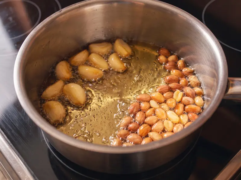 Salsa Macha: Knoblauchzehen und Erdnüsse bräunen in Öl im Topf auf dem Induktionsherd