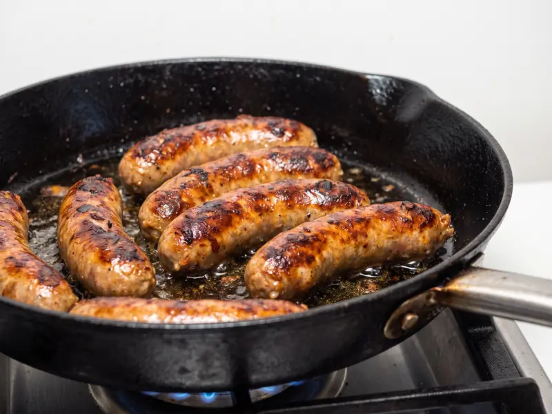 Italian sausages browned deep golden with blistered skin in the skillet