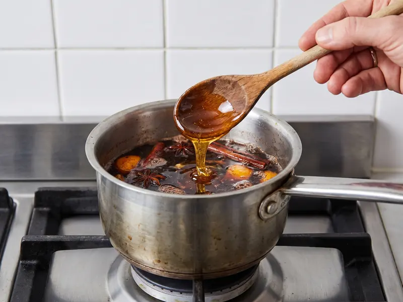 Miele dorato cola da un cucchiaio di legno nell'infuso scuro di spezie in un pentolino per lo sbiten