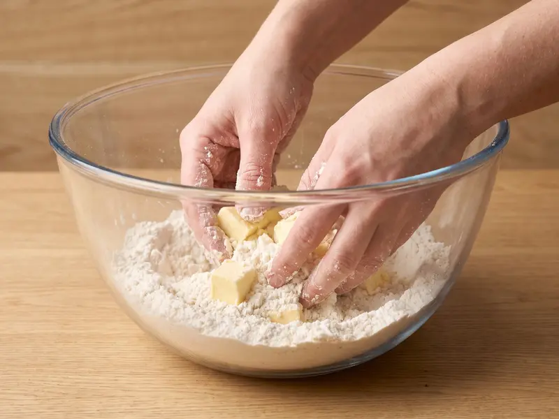 Cubetti di burro freddo sfregati con la farina con la punta delle dita in una ciotola di vetro, fino a briciole grossolane