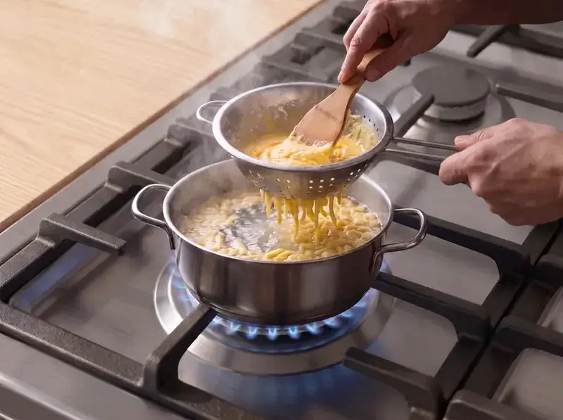 Spätzle: la pastella all'uovo passa da uno scolapasta nella pentola d'acqua che sobbolle