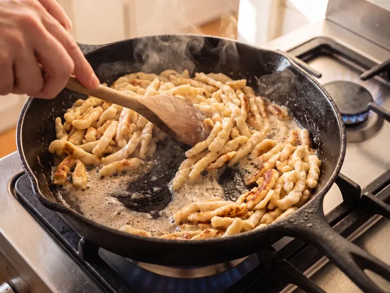 Spätzle saltati con una spatola di legno nel burro nocciola spumeggiante in padella di ghisa