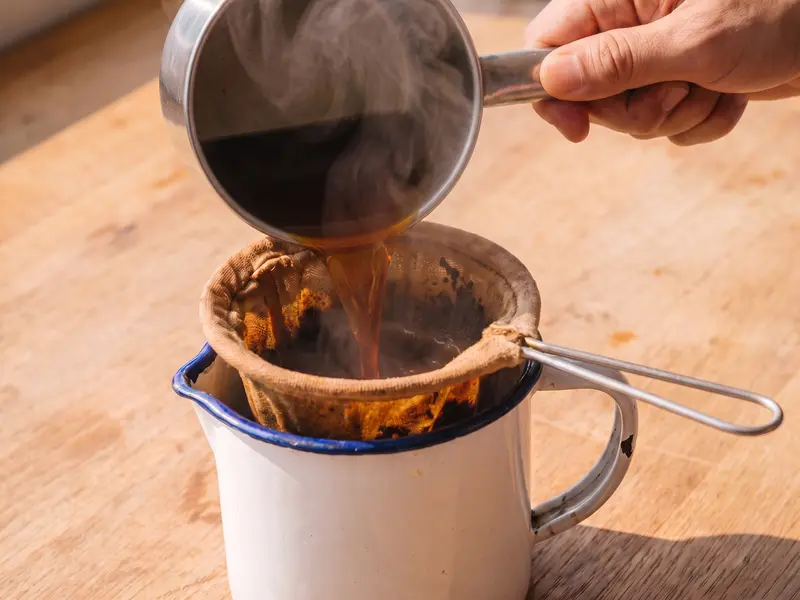 Brewed Thai tea strained through a cloth sock into a heatproof jug