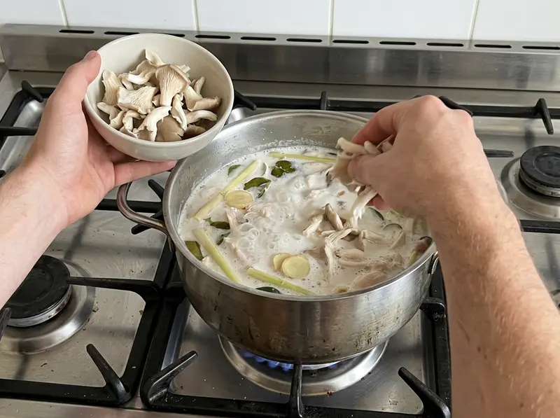 椰奶鸡汤:一只手把撕开的平菇放进有香茅、南姜和鸡肉的椰奶汤锅,另一只手端着一碗平菇