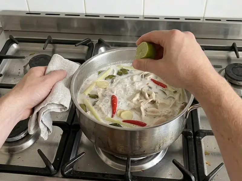 椰奶鸡汤:一只手把半个青柠挤进椰奶汤里,汤中有鸡肉、蘑菇、香茅和红辣椒
