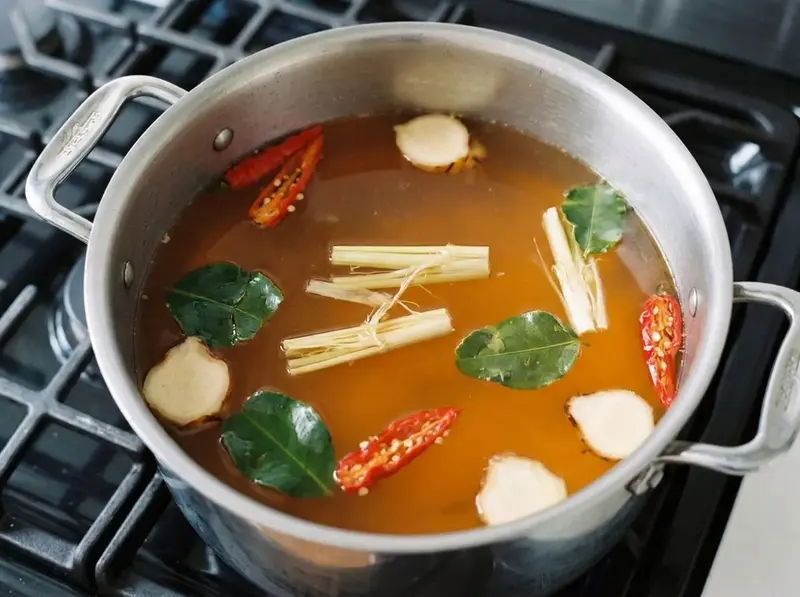 Tom yum goong: trozos de citronela abiertos, chiles rojos machacados, hojas de lima y galanga en caldo ámbar en una olla