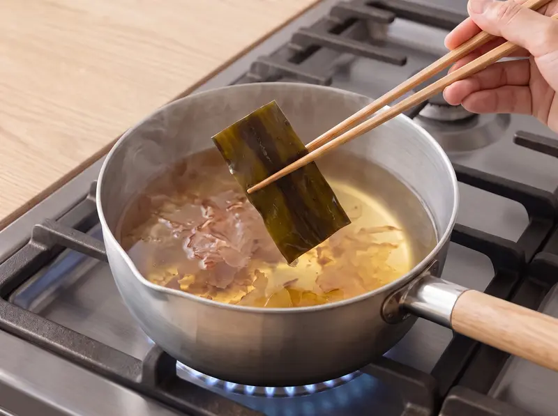 Unos palillos sacan el kombu del dashi caliente con copos de bonito, la base del kake udon