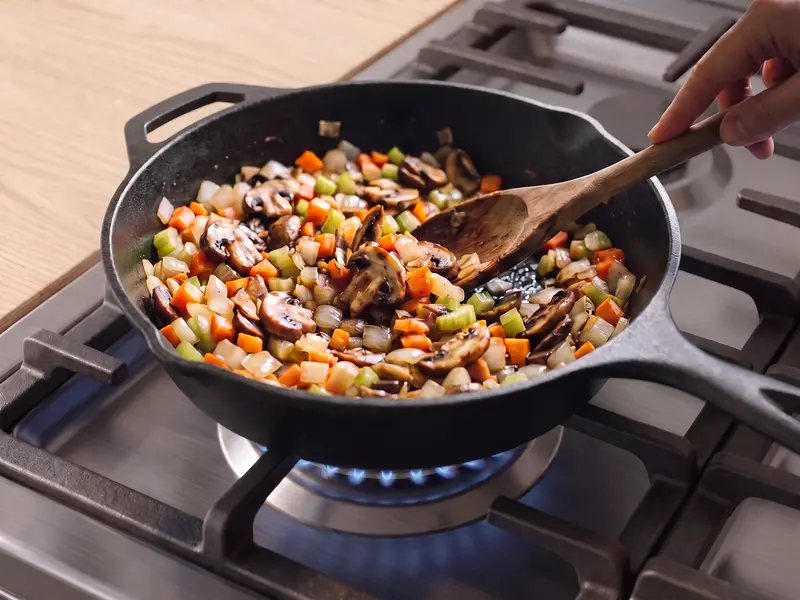 Cipolla, carota, sedano e funghi per lo shepherd's pie vegano rosolano in una padella di ghisa, mescolati a mano