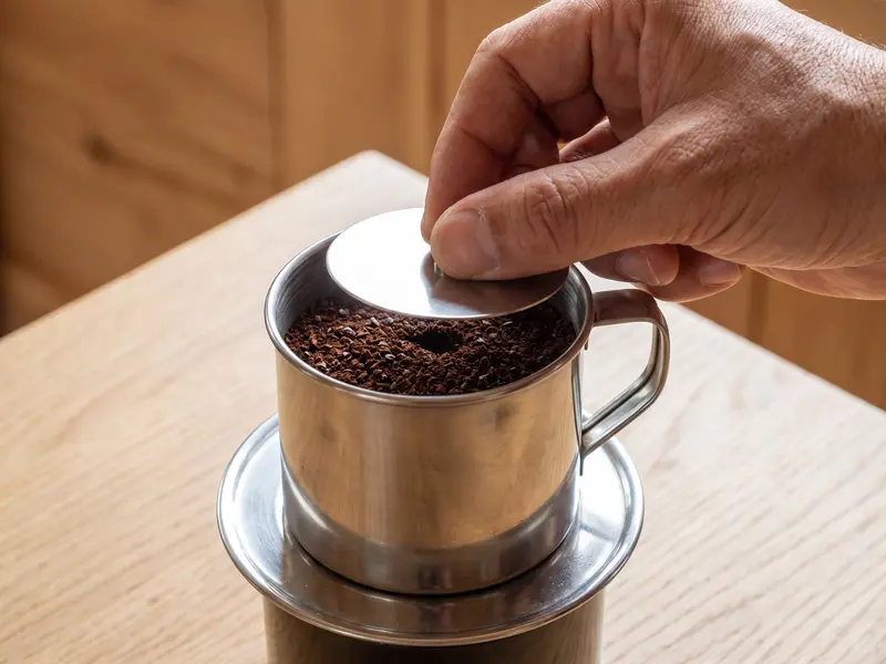 ベトナムアイスコーヒー用のステンレス製フィンに入れた黒いコーヒー粉の上にプレス板を置く