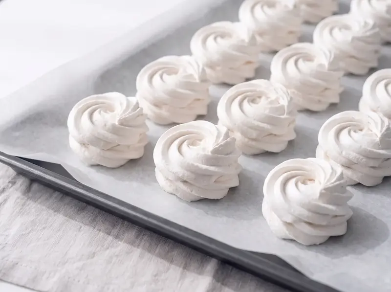 Rosette di zefir appena spremute che asciugano in file sulla carta forno, con le spirali in primo piano